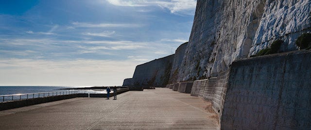 A wide concrete path overlooked by an imposing cliffside